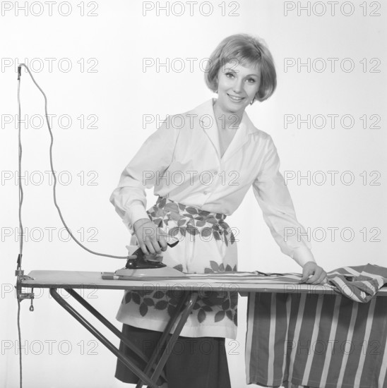 Ironing in the 1960s. A woman seen ironing curtains, smiling at the camera in the photographers studio. Sweden 1965. Conard ref 1743