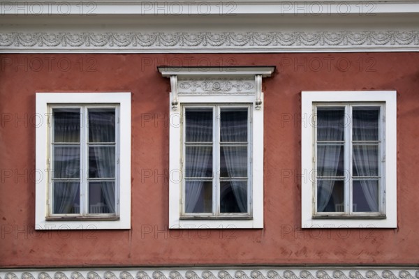 Detail of three windows on the exterior of a red, classic, historic city building in Helsinki, Finland. Light alterations in post production