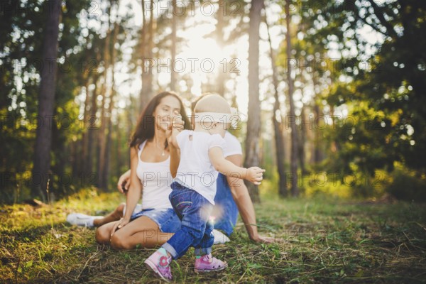 Young parents are taught to walk a daughter of one year on nature in a park on a lawn. The first steps of the child's hand with his mother and father