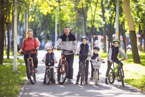 Theme family active sports outdoor recreation. A group of people is a big family of 6 people standing posing on mountain bikes in a city park on a road on a sunny day in autumn
