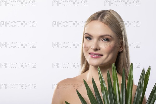A smiling woman poses with a vibrant tropical plant against a soft light backdrop, showcasing natural beauty