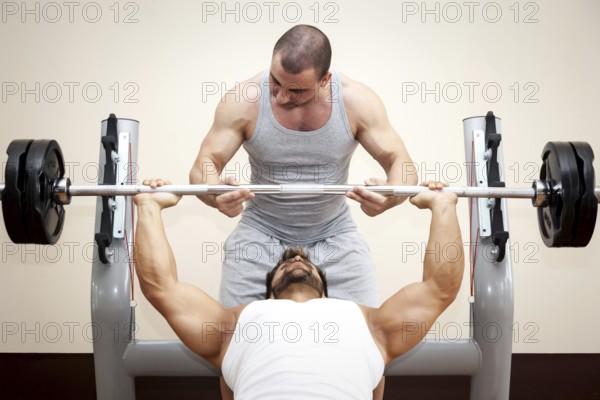 A handsome young muscular sports man doing bench press with a little help