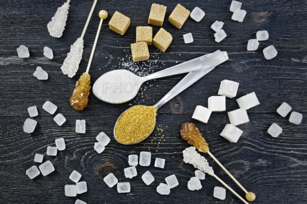Sugar white and brown granulated in spoons, crystal and cubes on the background of a black wooden board from above
