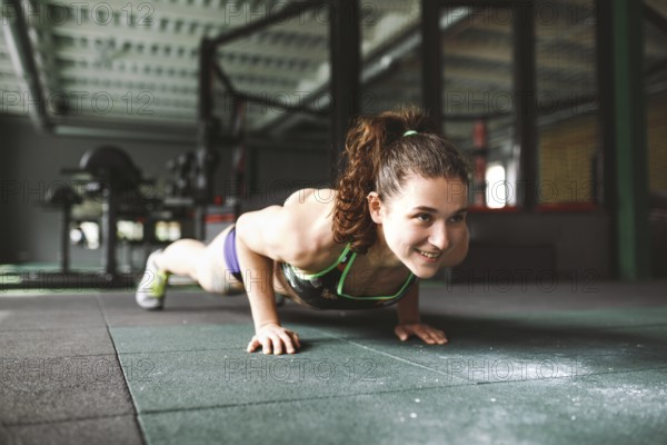 The girl does push-ups from the floor in the gym. Training muscles of the back, arms and press. Working with your weight