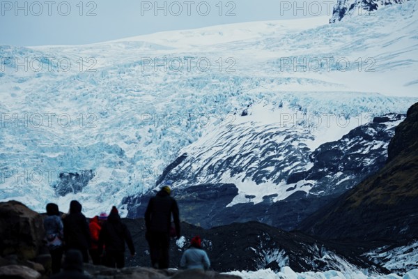 Group of tourists walking towards a large glacier under a cloudy sky, iceberg, glacier, snow, ice rock, ice diamont, glacier lagoon, nature, snow, diamont beach, Iceland, Europe