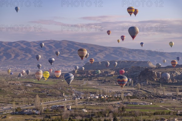 A picture of colorful hot air balloons flying over the landscape of Goreme Historical National Park at sunrise