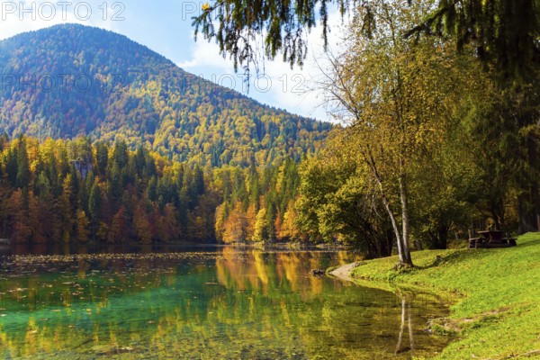 Orange, yellow and red trees are reflected in the green smooth water of the lake. Lake Fuzine. Magnificent colors of autumn