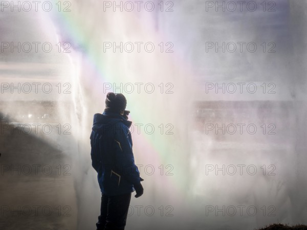 Male tourist in warm clothes standing behind huge majestic Seljalandfoss waterfall in Iceland
