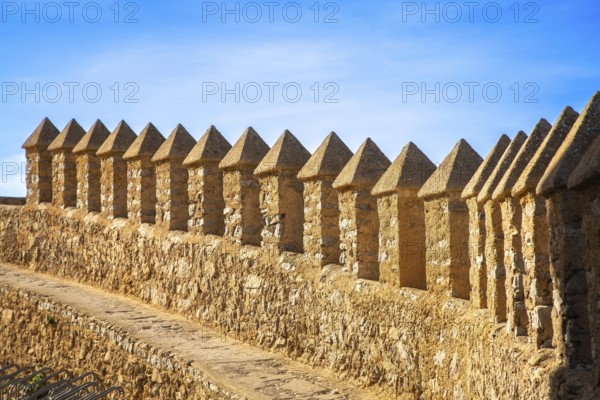 Long stone wall with regular battlements under a blue sky in sunlight, monastery with castle complex Santuari de Sant Salvador, Artà, Majorca, Spain, Europe