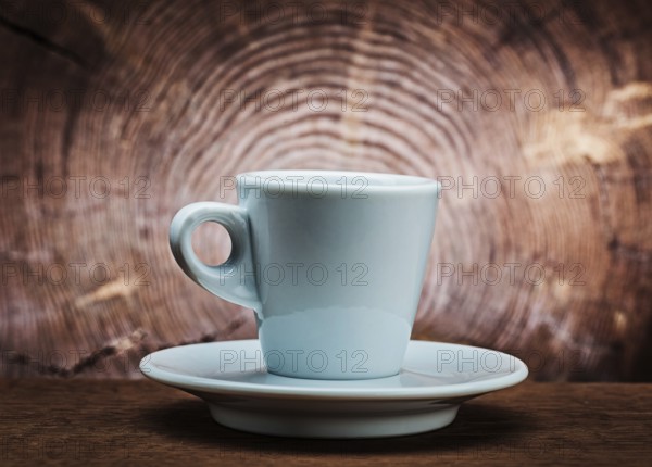White ceramic coffee cup on vintage wood background with cross cut of tree trunk