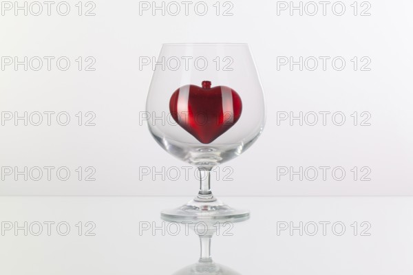 Red heart inside a glass of cognac on a glass plate