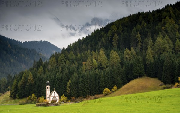 The small and beautiful church of Saint John, Ranui, Chiesetta di san giovanni in Ranui Runes South Tyrol Italy, surrounded by green meadow, forest and Dolomite mountains