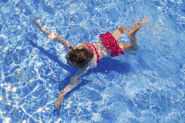 Bikini kid girl swimming on blue tiles pool in summer vacation