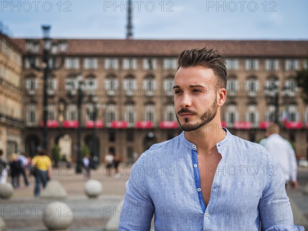 One handsome young man in urban setting in European city, standing, wearing shirt