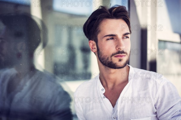 Stylish trendy young man standing outdoor against office window, looking confindent away