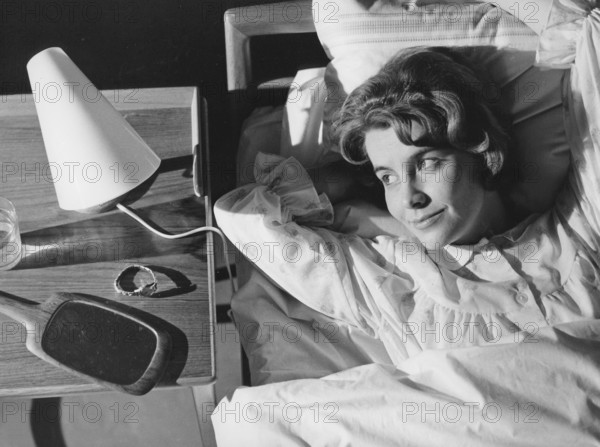 Sleep in the 1960s. A young woman lies comfortably ensconced in a bed. On the bedside table is a small reading lamp and a glass of water. Sweden 1960