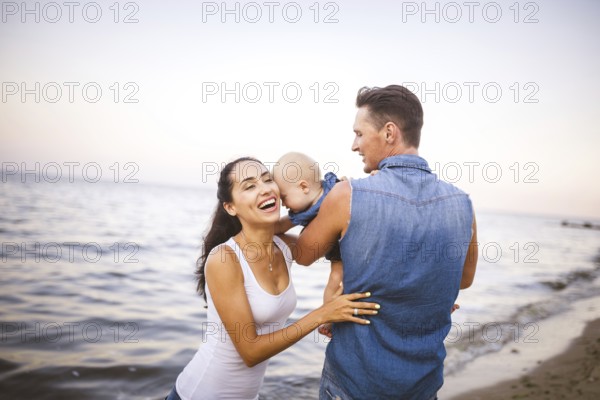 Beautiful young family on holiday with baby. The father holds the blonde girl in her arms, and the brunette's mother hugs her husband. The concept of a family beach holiday summer near the sea