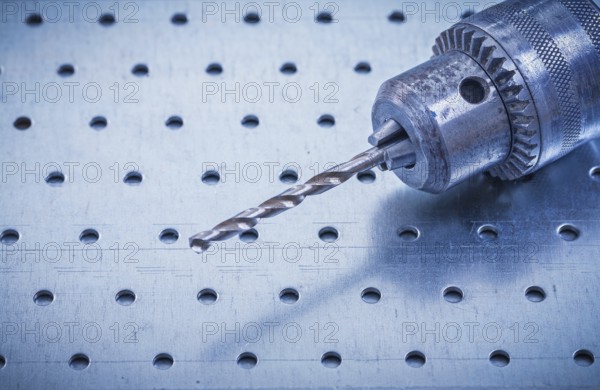 Metal drill on perforated metallic background construction concept