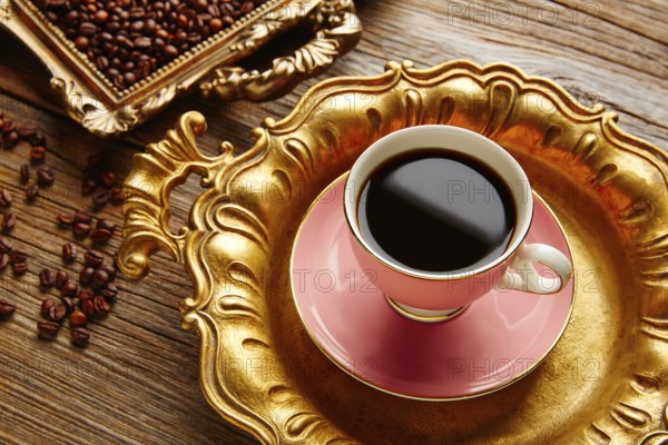 Coffee cup and beans on vintage golden tray in wooden old table