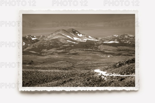 Landscape panorama, the partly snow-covered mountains of the Sierra Nevada rise on the horizon. Photo in sepia tones, white border with jagged edges in the character of old photos, horizontal shadow. Wide landscape panorama, on the horizon the partly snow-capped mountains of the Sierra Nevada rise. Photo in sepia tones, all around a white jagged edge in the character of old photos