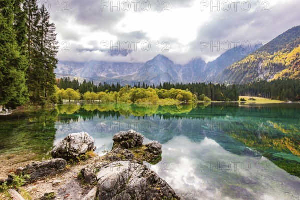 Gorgeous reflections. Picturesque lake Fusine in Northern Italy. Mountains covered in mist. The smooth surface of the water reflects the lush splendor of the surrounding forest and mountains