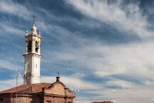 Historic church bell tower reaching out to a clear blue sky adorned with delicate clouds. Vigevano, Lombardy. Italy