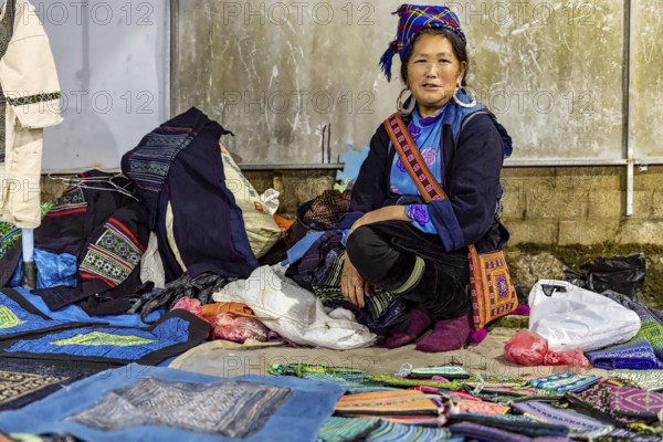 Woman in traditional dress presents handmade textiles at a lively market stall, The street market of Sa Pa in Vietnam