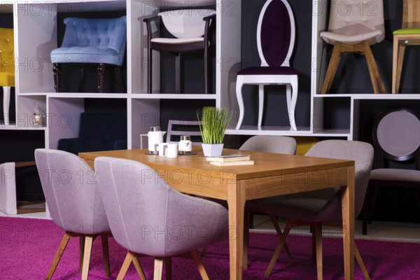 Shop, sale of furniture in a shopping centre. Exposure sample Dining wooden table with textile chairs in grey on a white shelf with furniture and a pink carpet