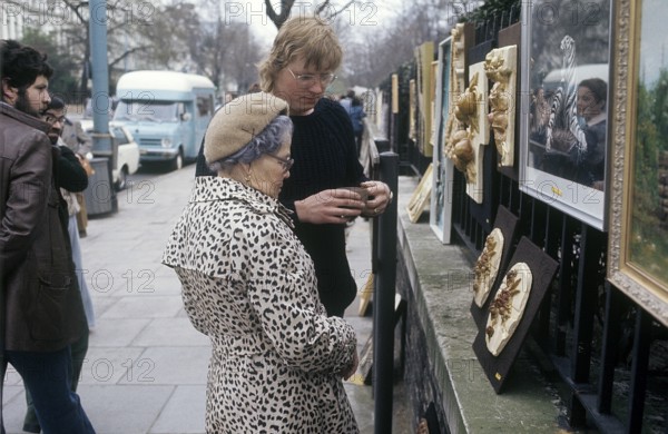 London 1982. A view from a London street with an elderly lady looking at art hanged on the fence to a park. Credit Roland Palm
