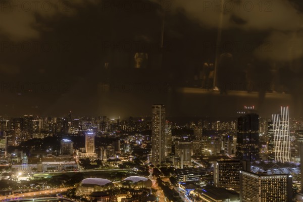 Singapore City, Singapore, January 23, 2019: Beautiful aerial night view of Marina Bay and the surrounding buildings. Reflections cause due to photo taken through window on observation deck, Asia