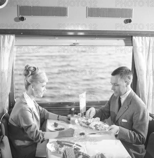 Train travel in the 1960s. A couple in the restaurant car of the train is enjoying dinner together. She has a typical 1960s hairstyle. 1964 Kristoffersson ref DD107-8
