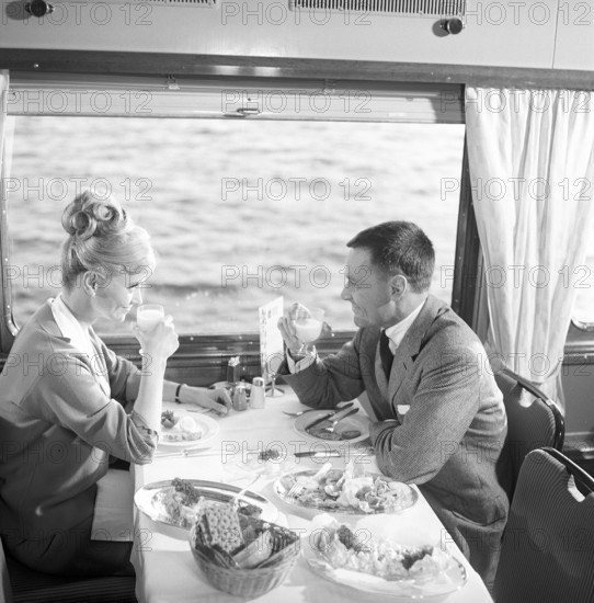 Train travel in the 1960s. A couple in the restaurant car of the train is enjoying dinner together. She has a typical 1960s hairstyle. Sweden 1960s Kristoffersson ref DD107-5