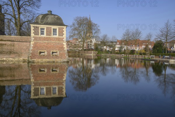 A pavilion at the moat with a clear reflection, surrounded by trees in the park in front of a blue sky, ahaus, münsterland, germany