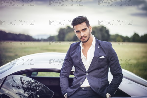 Portrait of young attractiave man in business suit sitting in his new stylish car outdoor in countryside