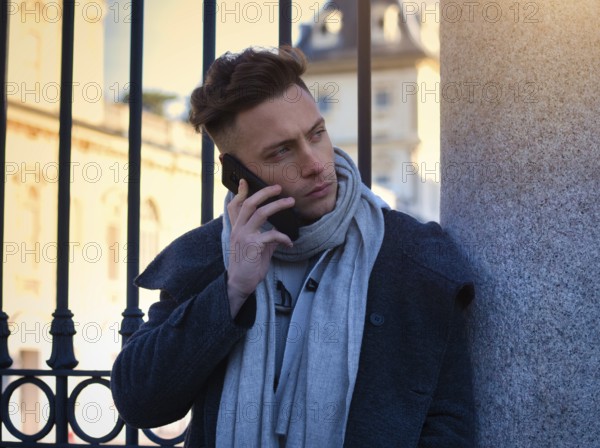 Handsome trendy man wearing white shirt standing and talking on cell phone, outdoor in city setting in day shot