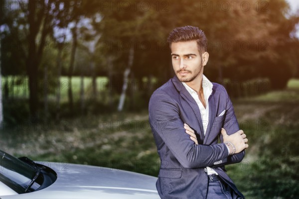Portrait of young attractiave man in white shirt leaning on his new stylish polished car outdoor