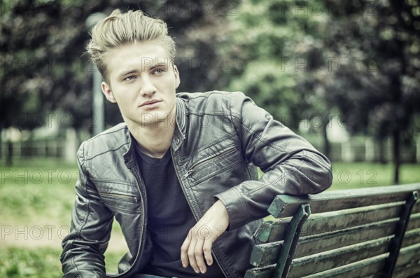 Handsome blond young man sitting on green, wooden park bench