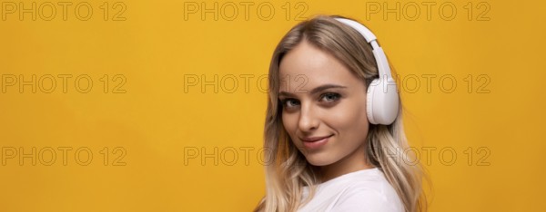 Smiling woman listening to music in white headphones on orange background with empty space