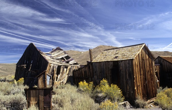 Windswept wooden houses in Bodie, collapsed by the weight of snow in winter. Colour photo, landscape format. Crooked, through snow load in winter squeezed wooden sheds in Bodie. Colour picture, horizontal format