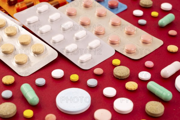 Different colorful pills and capsules in packs - blisters. Global pharmaceutical industry for billions dollars per year. Pharmaceutical drugs for use as medications. Isolated on a red background