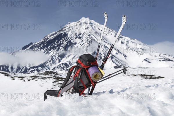 Equipment, backpack, skis and poles lie in snow on background cone of volcano on Kamchatka Peninsula on sunny day. Eurasia, Russian Far East, Kamchatka Region