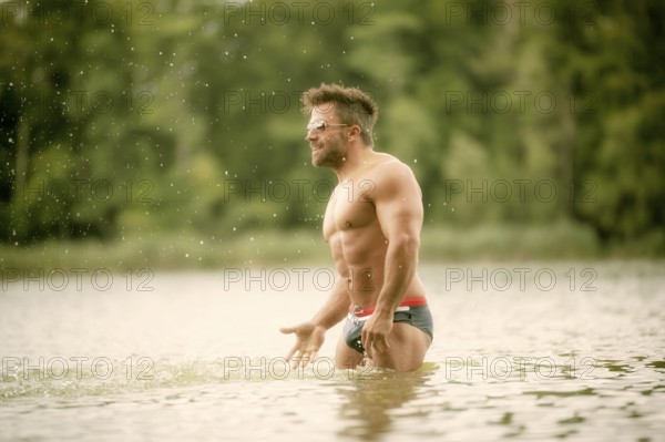 An image of a muscular man in the lake with a white shirt and sunglasses
