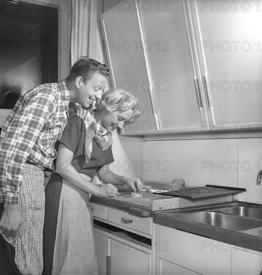 In the kitchen in the 1950s. Ayoung couple baking heart shaped gingerbread cookies for christmas. She puts the heartshaped metal form on the dough to make the shape. She is actress UllaCarin Rydén. Sweden 1951. ref Kristoffersson BE65-9