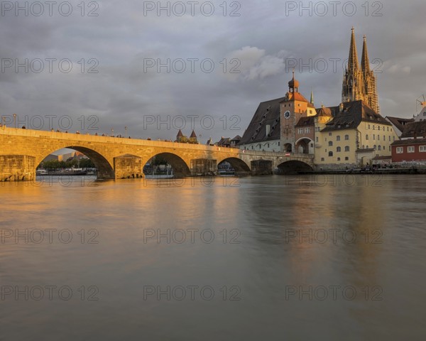Serene riverside scene at sunset with a bridge, cathedral, and historic town reflecting on the water, A stone bridge and cathedral at sunset reflecting in a calm river. Regensburg, Germany, Europe