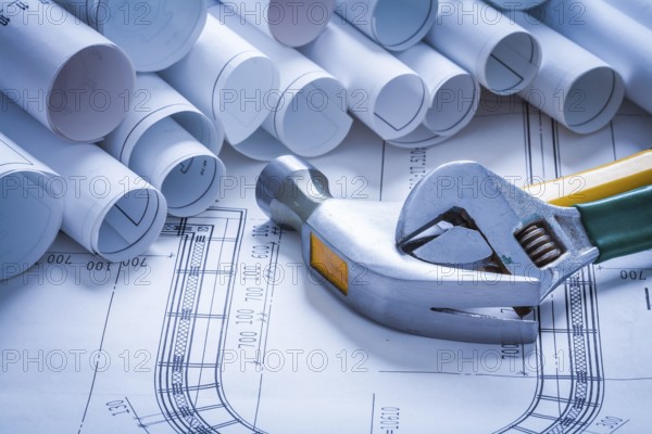 Claw hammer adjustable spanner and pile of blueprint rolls construction concept
