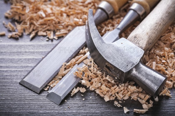 Close up of claw hammer and metal firmer chisels in wooden planning chips on vintage wood board construction concept