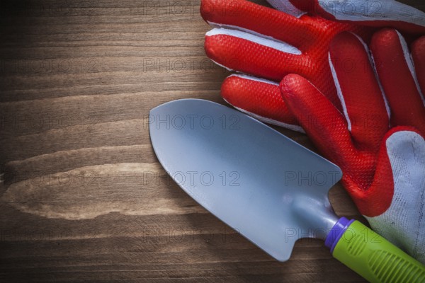 Safety gloves and metal trowel on wooden background