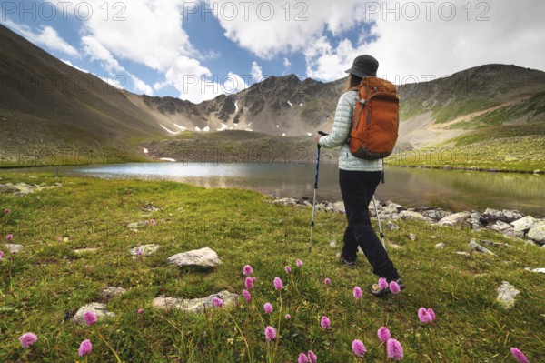 A woman with a backpack walks near the mountains and a blue lake. Travel and hobby concept