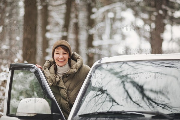 Cheerful female smiling and looking at camera while driving modern vehicle on blurred background of snowy countryside