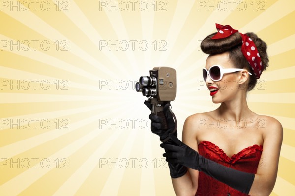 Vintage photo of glamorous pinup girl wearing a sexy red corset, shooting with an old retro cinema 8mm camera on colourful abstract cartoon style background